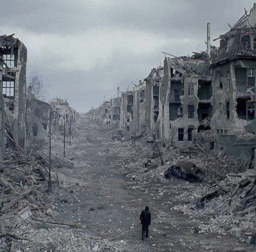 a film still showing a person walking through a desolate landscape of bombed buildings